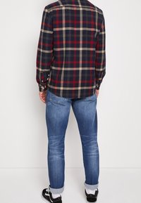 Koszula flanelowa w kratę w kolorach granatowym, czerwonym i beżowym z mankietami na dwa guziki. Zestawiona z jeansami o średnim odcieniu i czarnymi sneakersami.