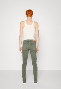 Jeans de corte ajustado en verde oliva con un diseño clásico de cinco bolsillos, un desgaste sutil y un parche de cuero de la marca en la parte trasera de la cintura.