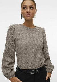 Maglione grigio texturizzato a maniche lunghe con spalle a sbuffo, scollatura rotonda e una vestibilità leggermente cropped, abbinato a una cintura nera e pantaloni.