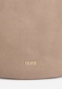 Borsa in suede beige con una texture liscia e una forma arrotondata. Presenta un logo in rilievo dorato "TCLASSE" sulla parte inferiore.