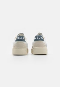 Sneaker bianchi e beige con un accento blu, dotati di una tomaia in pelle liscia, tallone in suede beige e suola in gomma testurizzata.