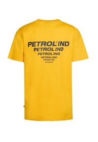 Camiseta de algodón amarilla de manga corta, con el texto en negrita negro "PETROL IND" impreso múltiples veces en la parte posterior.