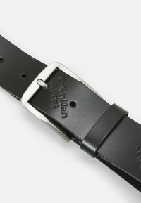 Cintura in pelle nera con fibbia in metallo argentato. Presenta pelle testurizzata e marchio inciso. Dotata di più fori per la regolazione.