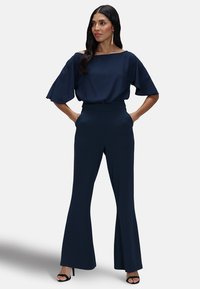 Marineblauwe off-shoulder top met vlindermouwen, gecombineerd met hoge taille wijde broek. Vezelachtige stof, minimalistisch ontwerp.