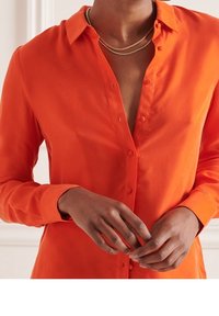 Langærmet skjorte med knapper i klar orange, lavet af glat stof. Har en klassisk krave og subtil glans, med en slank pasform.