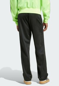 Pantalons de sport noirs en tissu lisse avec une coupe décontractée, comportant des bandes latérales et une taille à cordon. Accentué d'un haut contrastant.