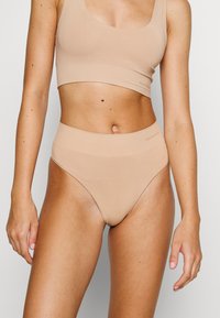 Beige high-waisted underwear and matching crop top made of smooth fabric. Features a seamless design with a subtle brand logo.
