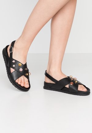 Czarne skórzane sandały z krzyżującymi się paskami, ozdobione kolorowymi ćwiekami, z płaską gumową podeszwą i tylnym paskiem.