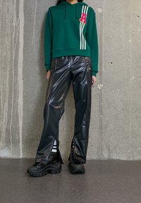 Felpa verde con strisce bianche e lettera A rosa, abbinata a pantaloni neri in finta pelle lucida con zip laterali e stivali neri chunky.
