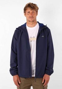 Veste légère bleu marine avec capuche, poignets élastiques et fermeture éclair à l'avant. Portez-la par-dessus une chemise blanche avec un design graphique simple.