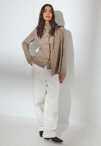 Bežs adīts kardigans ar zelta pogām, apvienots ar baltām platu kāju biksēm un melniem potīšu zābakiem. Kardigans krīt ar ribota akcentiem.