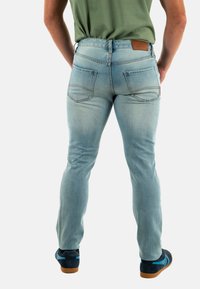 Jeans in denim blu chiaro con vestibilità slim, dotati di due tasche posteriori e un'etichetta in pelle marrone in vita. Il materiale sembra morbido.