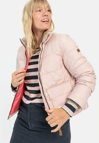 Gevoerde roze jas met een hoge kraag, rits aan de voorkant en twee zijzakken; heeft een contrasterende rode binnenvoering en bruine accenten.