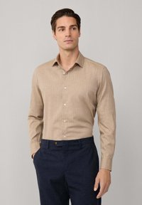 Lichtbruine blouse met lange mouwen en een knoopsluiting, gecombineerd met donkere, gebloemde broeken. Soepele stofstructuur, klassieke kraagstijl.