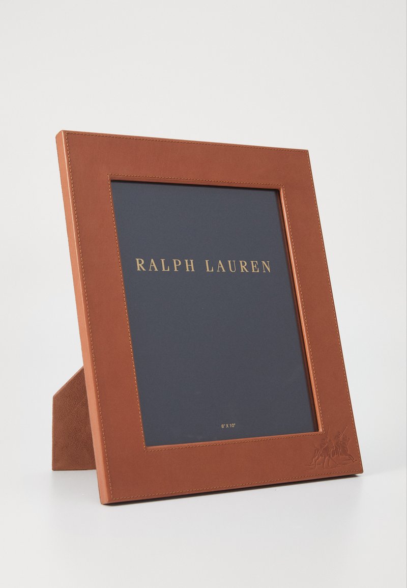 Brūns ādas foto rāmis ar teksturētu virsmu, kurā ir zelta burti un reljefa dizains. Tur 8"x10" fotogrāfijas.