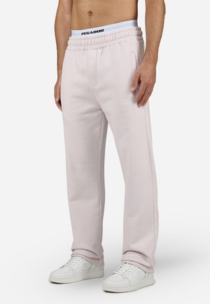 Pantalons de sport rose clair avec une taille élastique, des poches latérales et un logo 'PEGADOR' brodé en blanc. Portés avec des baskets blanches.