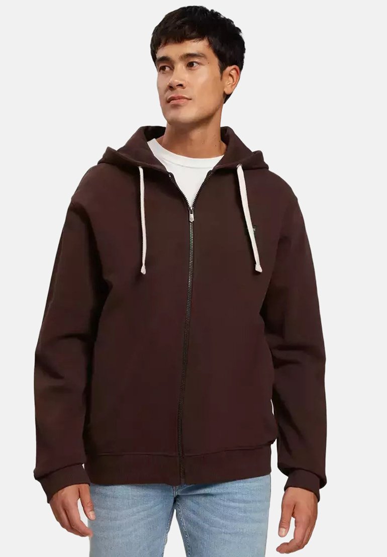 Brązowa bluza z kapturem na zamek błyskawiczny, z regulowanym kapturem, z przodu na zamek oraz ściągaczami przy mankietach i u dołu. Nosi się ją na białej koszuli, w połączeniu z jasnymi dżinsami.