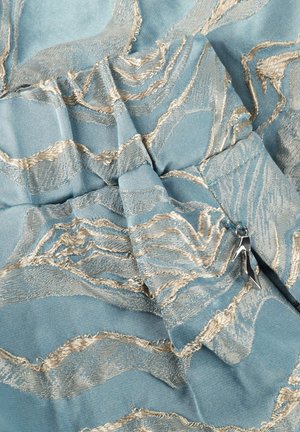 Blauwe stof met beige, textuurrijke borduurwerk en een klein zilveren hangertje in de vorm van een hoge hak, bevestigd bij een geplooide naad.