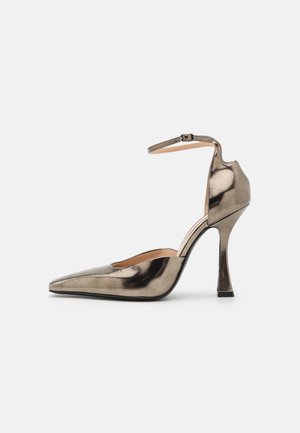 Chaussure à talons hauts grise métallique avec un bout pointu, une sangle à la cheville et un design de talon angulaire unique. Texture lisse avec un éclat subtil.