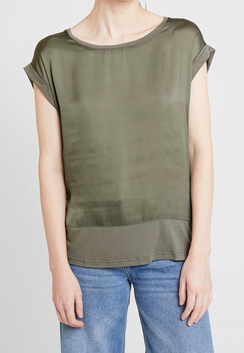 Top de manga corta en verde oliva, material satinado, corte relajado, escote en forma de pico, mangas con dobladillo enrollado y dobladillo ligeramente más largo en la parte trasera.