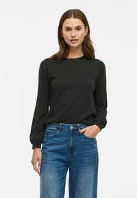 Top negru cu mânecă lungă, guler rotund și detalii pliate la umeri, asortat cu blugi albastri cu talie înaltă, cu un design clasic cu cinci buzunare.