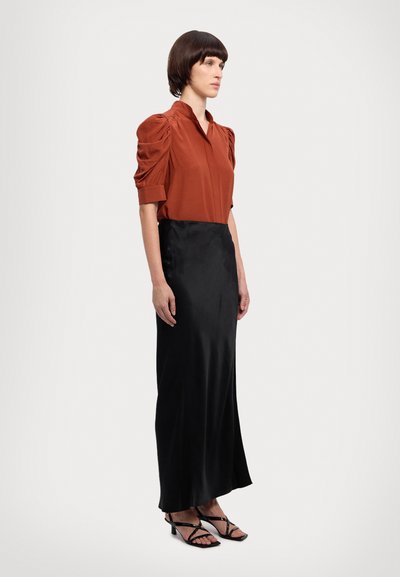 Rustfarvet bluse med pufærmer, parret med en glat sort satin-maxikjole. Har strappy sorte sandaler. Glatte teksturer hele vejen igennem.