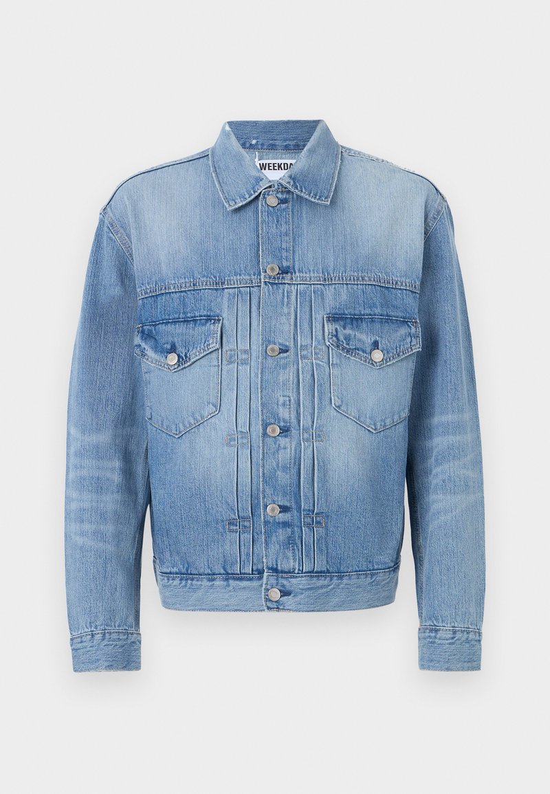 Veste en denim bleu clair avec deux poches poitrine, boutons en métal argenté et col classique. Présente une texture délavée et une coupe ajustée.