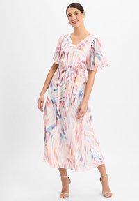 Floral-patterned maxi dress in light, sheer fabric with flutter sleeves, V-neckline, cinched waist, and pastel colors. Silver heeled sandals.