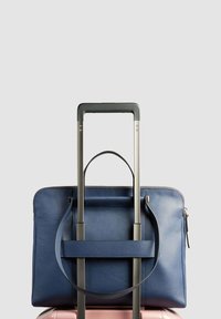 Blauwe leren laptoptas met een enkele bovenhandgreep en ritssluiting, geplaatst op een roze koffer, beveiligd door een uitschuifbare handgreep.