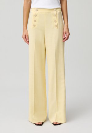 Pantaloni palazzo in morbido tessuto giallo con una texture liscia. Presentano grandi bottoni rotondi su ciascun lato e un design a vita alta.