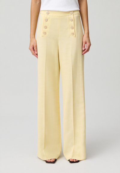 Pantalons à jambes larges en tissu jaune doux avec une texture lisse. Doté de grands boutons ronds de chaque côté et d'une taille haute.