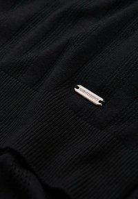 Black knit fabric with textured stripes, featuring a small metallic label with the text “@QUINTESSENCE.” Surface is smooth and matte.