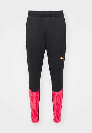Pantaloni sportivi neri con finitura texturizzata, caratterizzati da accenti di motivo geometrico rosa sulle gambe inferiori e un logo giallo di lato.