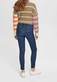 Jeans ajustados de talle alto en azul oscuro con bolsillos traseros sutiles, combinados con un suéter corto de mezcla de lana con rayas multicolores.