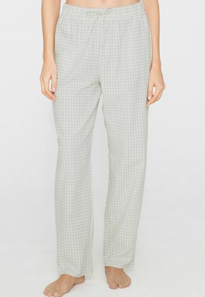 Hellgraue und weiße Gingham-Feinmuster-Pyjama-Hose mit Kordelzug, barfuß getragen von einer stehenden Person, sichtbar von der Taille bis zu den Füßen.