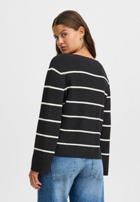 Juoda stripe dėvėtas megztinis su baltomis horizontaliomis linijomis, supplies tekstūra, platus kaklo iškirpimas ir ilgomis rankovėmis, derinamas su m�ėlynais džinsais.