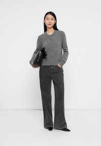 Cardigan en laine gris avec un col rond et une fermeture à boutons, associé à un jean noir à jambes larges et à une pochette noire.