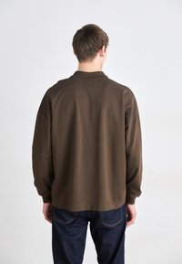 Brun genser med krage og senkede skuldre, laget av mykt materiale. Kombinert med mørkeblå jeans med subtile sømdetaljer.