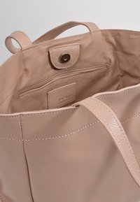 Beige läder tote-väska med dubbla remmar, inre dragkedjefack, tryckknapps-stängning och en liten logotypmärkning inuti.