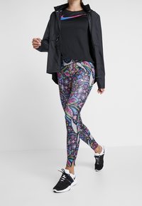 Chaqueta ligera negra, camiseta negra de Nike con logo rosa, leggings coloridos con patrones florales y geométricos, zapatillas negras.