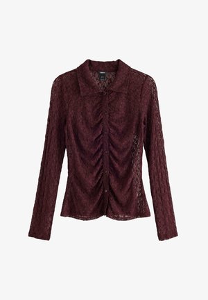Bordeaux spetsblus med långa ärmar, rynkad frontdetalj och knappstängning. Har en klassisk krage och ett texturerat blommönster.