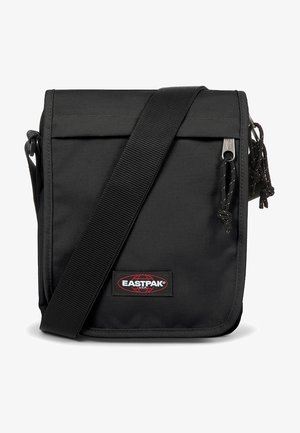 Musta kangasta valmistettu olkalaukku, jossa on säädettävä hihna, käännettävä läppä, hopeinen vetoketju ja Eastpak-logopatchi edessä.