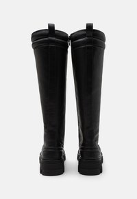 Černé kožené kozačky až ke kolenům s kulatou špičkou, plochou gumovou podrážkou, bočními zipy a přehnutými lemy. Texturovaný povrch s vertikálními švy.