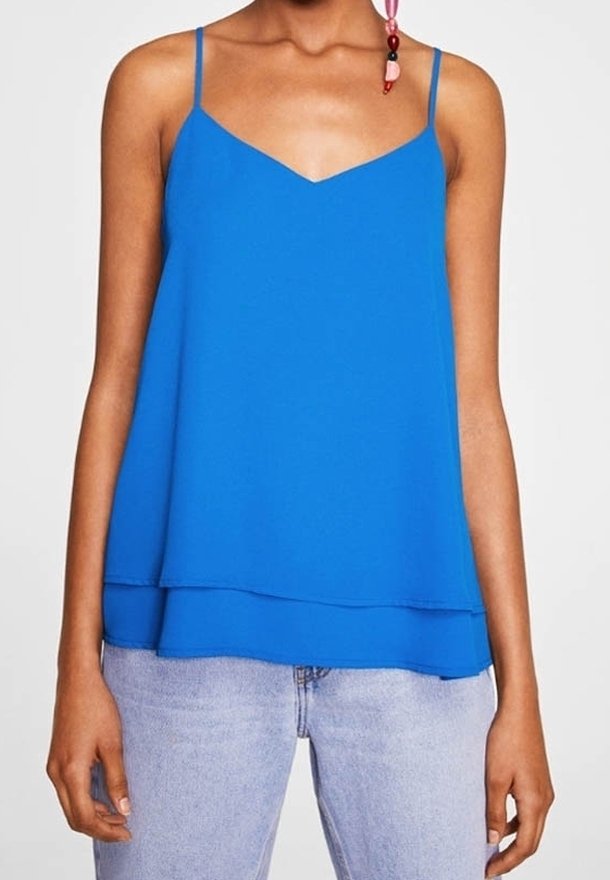 Haut sans manches bleu avec des bretelles fines, décolleté en V, design superposé et texture lisse. Assorti avec un jean bleu clair.
