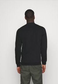 Sudadera negra de manga larga con puños y dobladillo acanalados, que presenta un cuello redondo y costuras acentuadas. Combinada con pantalones de color verde oliva.