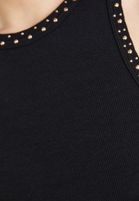 Detailní záběr na černý žebrovaný top bez rukávů s kulatým výstřihem, zdobený malými kovovými nýty.