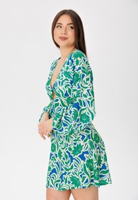 Vestido mini floral en verde y azul con mangas largas, escote en V pronunciado y falda fluida, que presenta una tela estampada y un corte holgado.