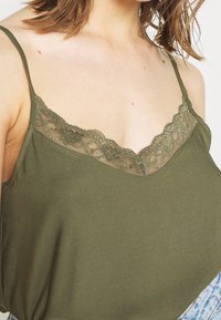 Olive green camisole top with lace trim along the neckline, featuring thin adjustable straps and a soft, smooth fabric texture.