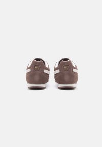 Sapatos de camurça castanha com acentos têxteis brancos e sola de borracha. Apresenta um logo no calcanhar e um detalhe de costura em contraste.