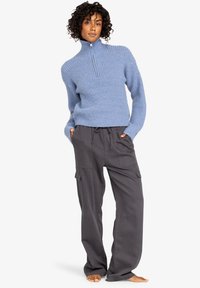 Světle modrý žebrovaný pletený svetr s vysokým límcem a šedé cargo kalhoty s kapsami, volný střih a stahovací pas.